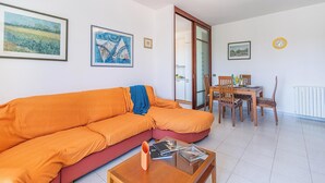 Una sala de estar con un sofá modular, una mesa de comedor con sillas, y una cocina visible a través de una puerta abierta.
