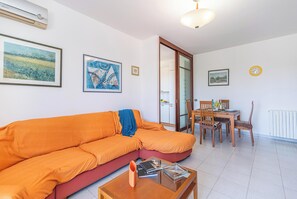 A living room with a sectional sofa, a dining table with chairs, and a kitchen area visible through an open door.