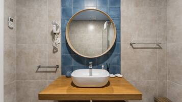 Een badkamer met een houten wastafelmeubel, een ronde spiegel, een witte wasbak en een blauwe betegelde muur.