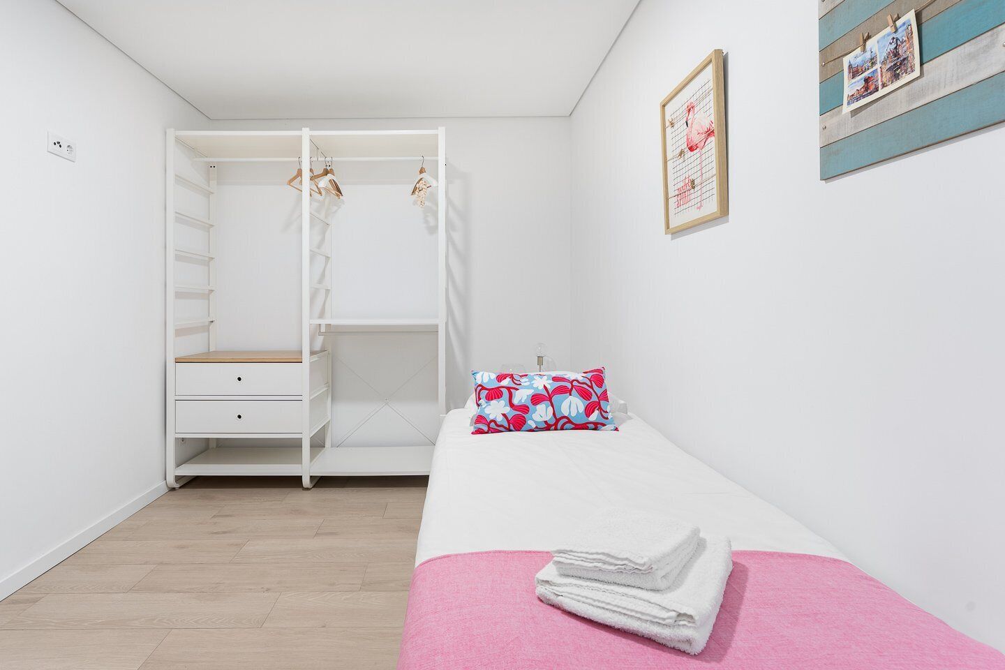 A bedroom with a bunk bed, a bedside table, a pink blanket, and a framed picture on the wall.