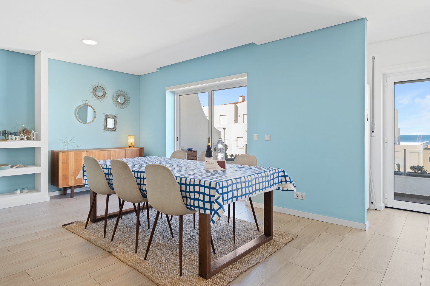 Een eetruimte met een tafel gedekt voor vier personen, een houten kast en decoratieve spiegels aan de muur.