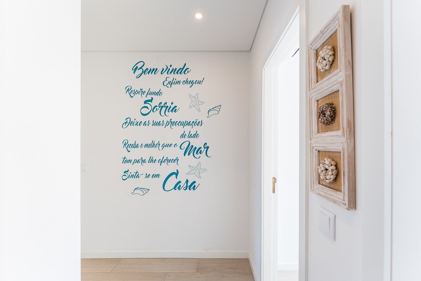 A wall with a decorative message in a foreign language, a wooden door with a rustic design, and a light-colored floor.