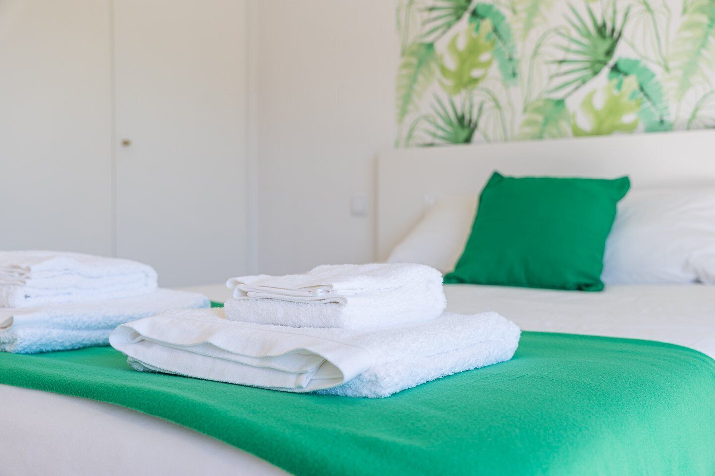 A neatly made bed with white and blue towels, a green throw blanket, and a green pillow on a white headboard.