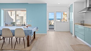 A modern kitchen with light blue cabinets, a dining area with a checkered tablecloth, and a view of the sea through the windows. - GuestReady - Relaxing escape near the beach (Moledo)