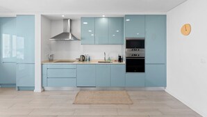 A modern kitchen with light blue cabinets, a stainless steel range hood, a built-in oven, and a clock on the wall. - GuestReady - Relaxing escape near the beach (Moledo)