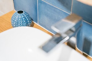 Une salle de bain avec un lavabo blanc, un vase bleu à motifs et un robinet métallique.