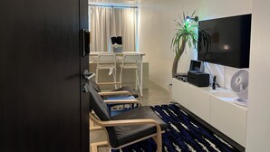 Un salon moderne doté d’un téléviseur à écran plat, d’un coin repas avec une table et des chaises, et d’une grande plante en pot.