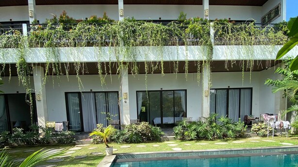 A modern building with a swimming pool, surrounded by lush greenery and a well-maintained lawn. - D Krisna Guest House (Canggu)