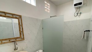 A modern bathroom with a marble-tiled wall, a white sink, a toilet, and a glass-enclosed shower area. - D Krisna Guest House (Canggu)