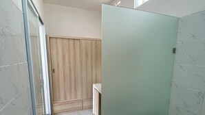 A bathroom with a glass shower door, a wooden vanity, and a small window. - D Krisna Guest House (Canggu)