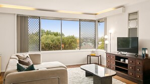 A modern living room with a sofa, a glass coffee table, a TV, and a wooden cabinet. - Designed Stay-Convenient, Coastal, Comfortable (Karrinyup)