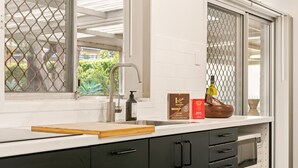 A kitchen with a stainless steel sink, a wooden cutting board, a bottle of olive oil, and a box of coffee. - Designed Stay-Convenient, Coastal, Comfortable (Karrinyup)