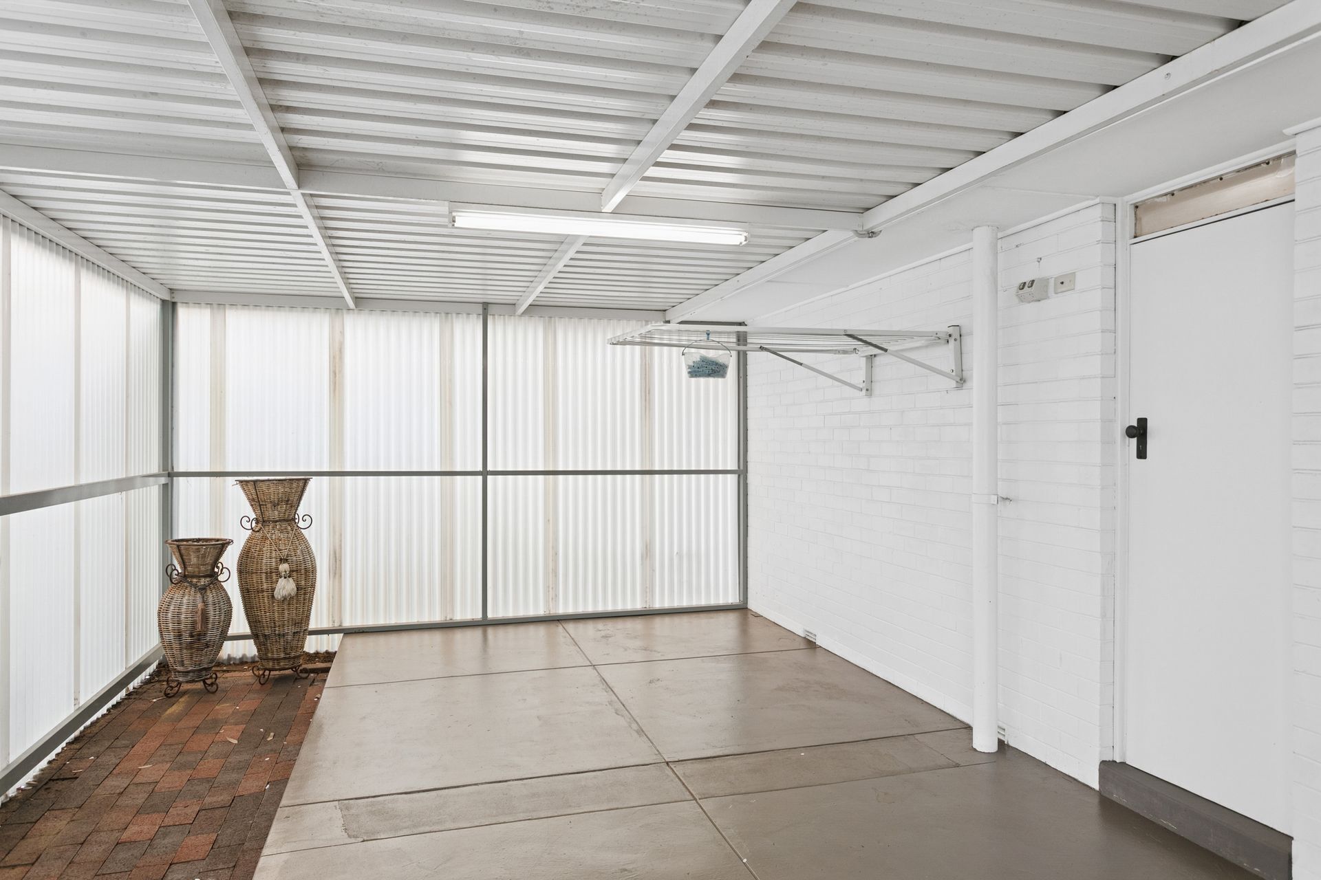 A corridor with a tiled floor, white walls, and a metal ceiling. There are two wicker baskets and a metal drying rack.