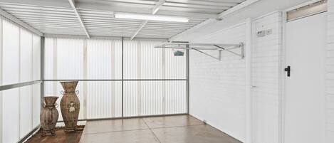 A corridor with a tiled floor, white walls, and a metal ceiling. There are two wicker baskets and a metal drying rack.