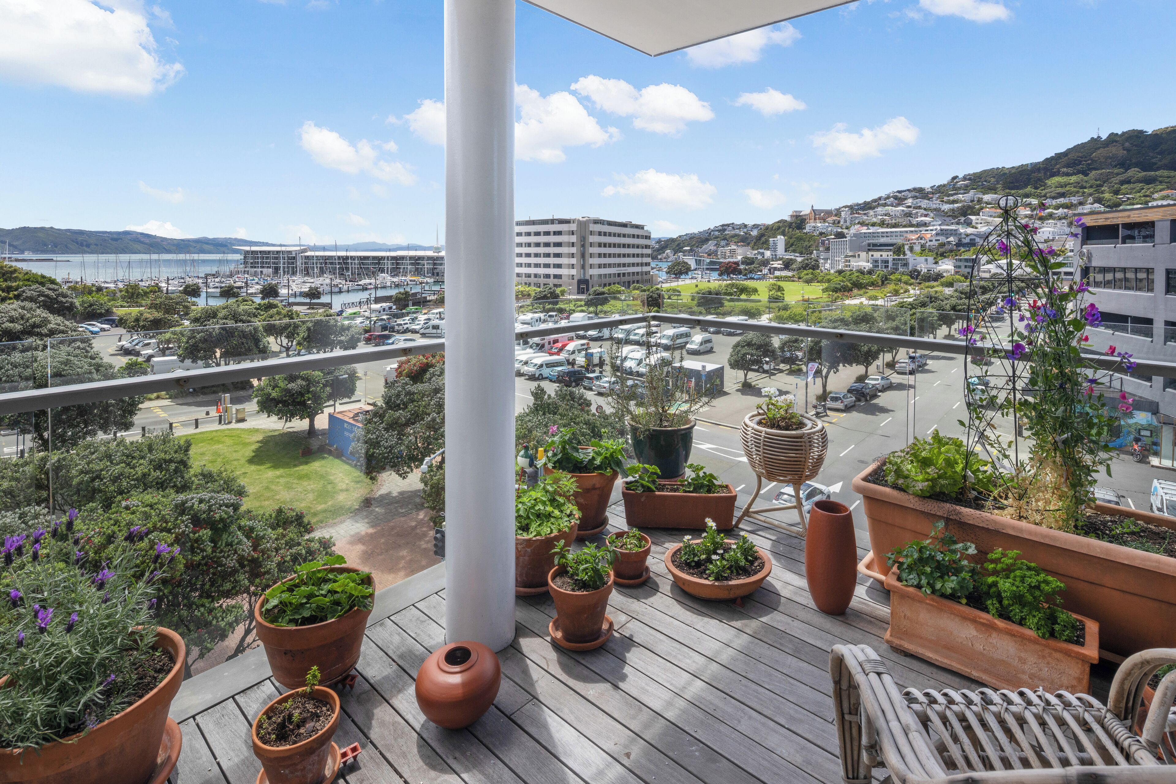 A balcony with potted plants, a view of a cityscape, and a clear sky.