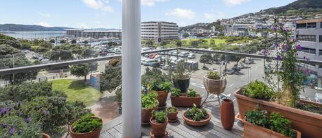 A balcony with potted plants, a view of a cityscape, and a clear sky.