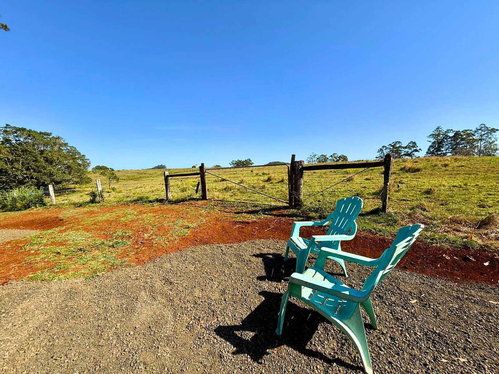 A rural setting with a dirt path leading to a wooden fence and a green plastic chair.