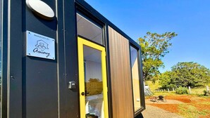 A compact, modern mobile home with a wooden deck and a yellow door, managed by Tiny Away. - Kalm The Farm 1 by Tiny Away (Numulgi)
