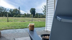Eine Tasse Kaffee auf einer Bank vor einem Gebäude, im Hintergrund eine Wiese und Bäume.