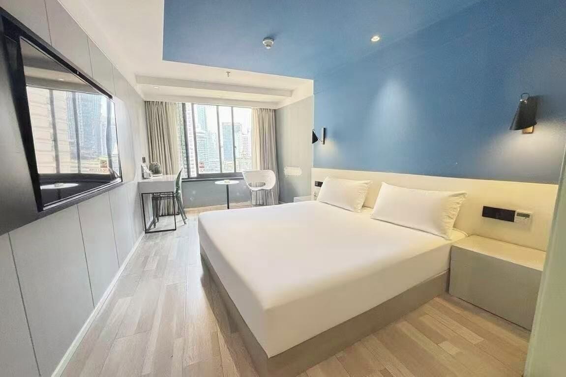 A modern hotel room with a large bed, a desk, and a view of the city.