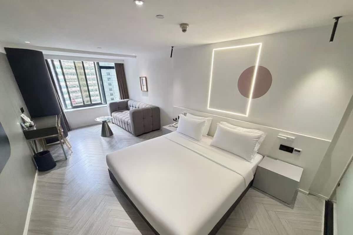Ein modernes Hotelzimmer mit einem großen Bett, einer Couch, einem Schreibtisch und einem großen Fenster.