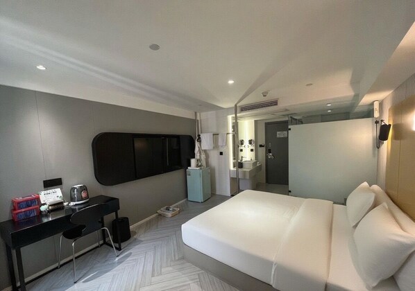 Una habitación de hotel moderna con una cama grande, un escritorio con una silla, una mesita y un espejo.