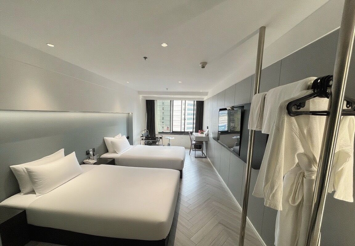 A hotel room with two beds, a TV, a desk, and a bathroom with a towel rack.