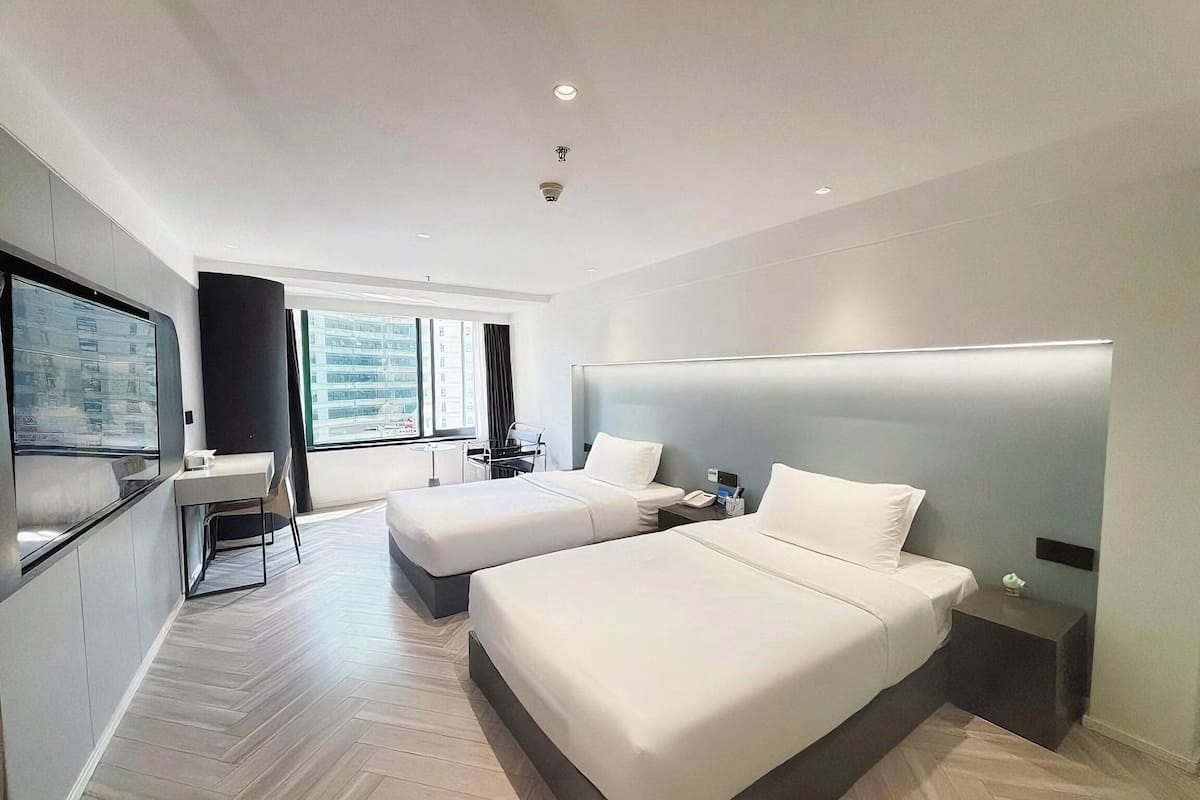 Ein modernes Hotelzimmer mit zwei Betten, einem Schreibtisch, einem Flachbildfernseher und einem großen Fenster mit Blick auf die Stadt.
