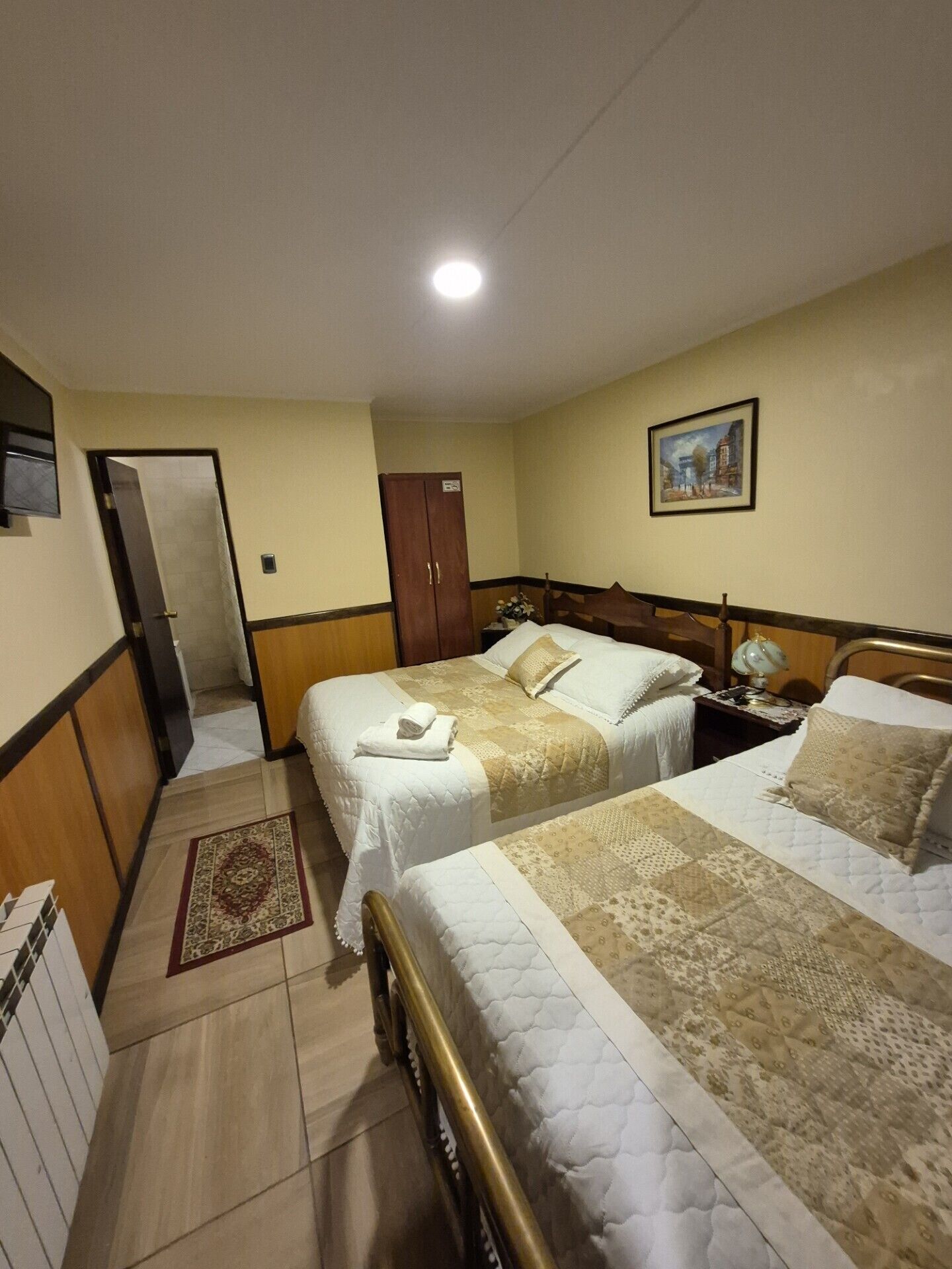 A hotel room with two beds, a wardrobe, a desk with a lamp, and a painting on the wall.
