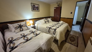 A hotel room with two beds, a nightstand with a lamp, a wardrobe, and a framed picture on the wall. - Hostal Oasis (Puerto Natales)