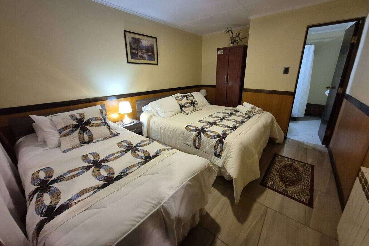 A hotel room with two beds, a nightstand with a lamp, a wardrobe, and a framed picture on the wall.