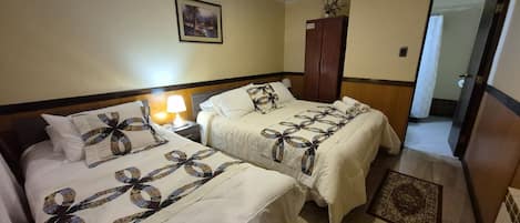 Habitación de hotel con dos camas, una mesita de noche con lámpara, un armario y un cuadro en la pared.