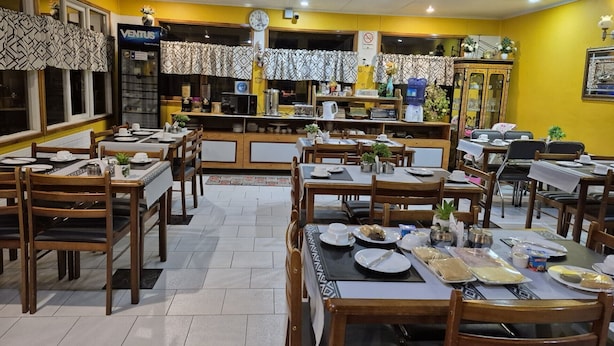 A restaurant with multiple tables and chairs, a clock, and a vending machine. - Hostal Oasis (Puerto Natales)