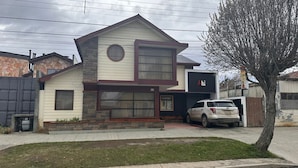 A two-story house with a stone facade, a garage, and a parked car. - Hostal Oasis (Puerto Natales)