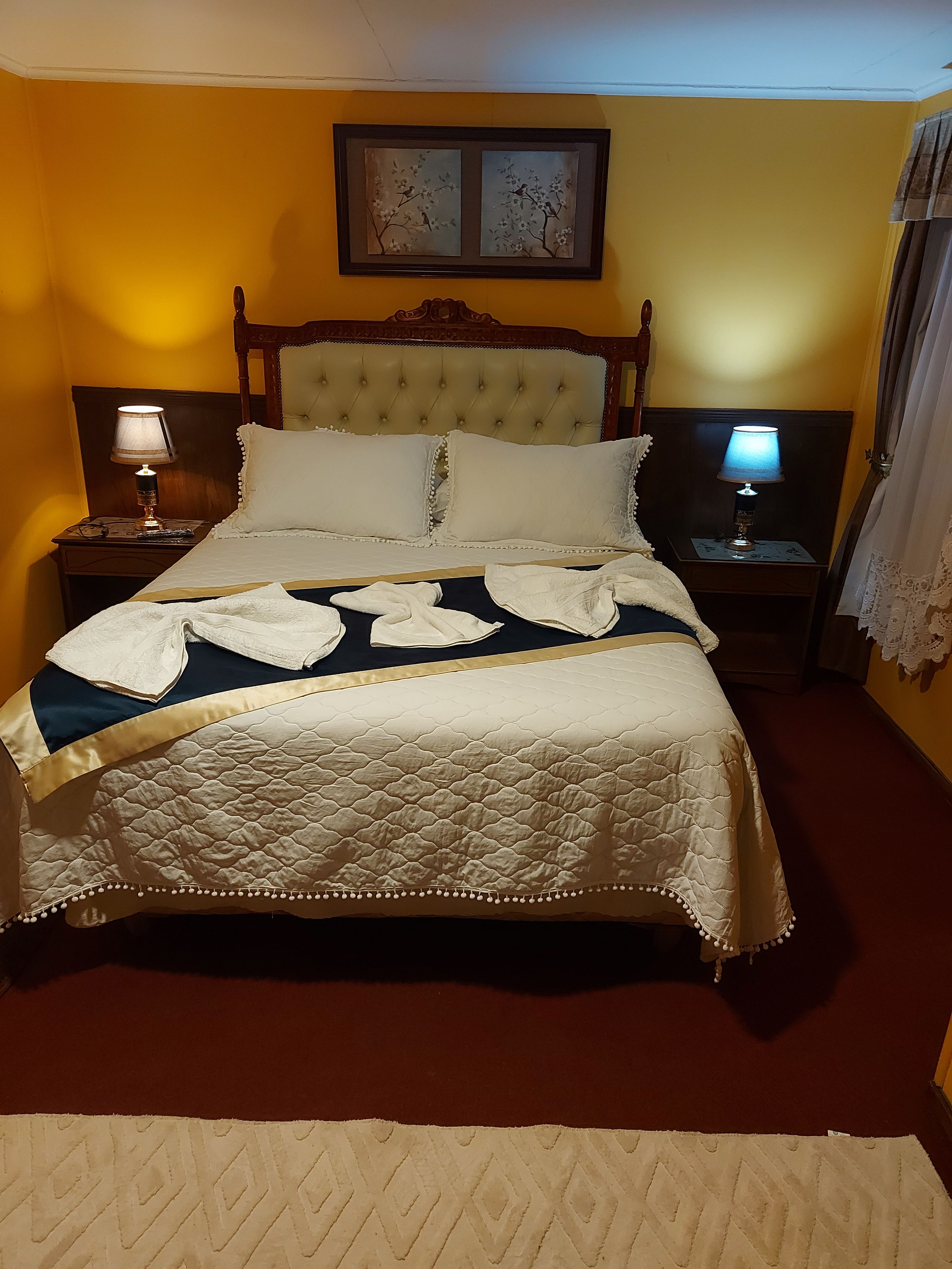 A bed with a quilt, two nightstands with lamps, a framed picture on the wall, and a window with curtains.