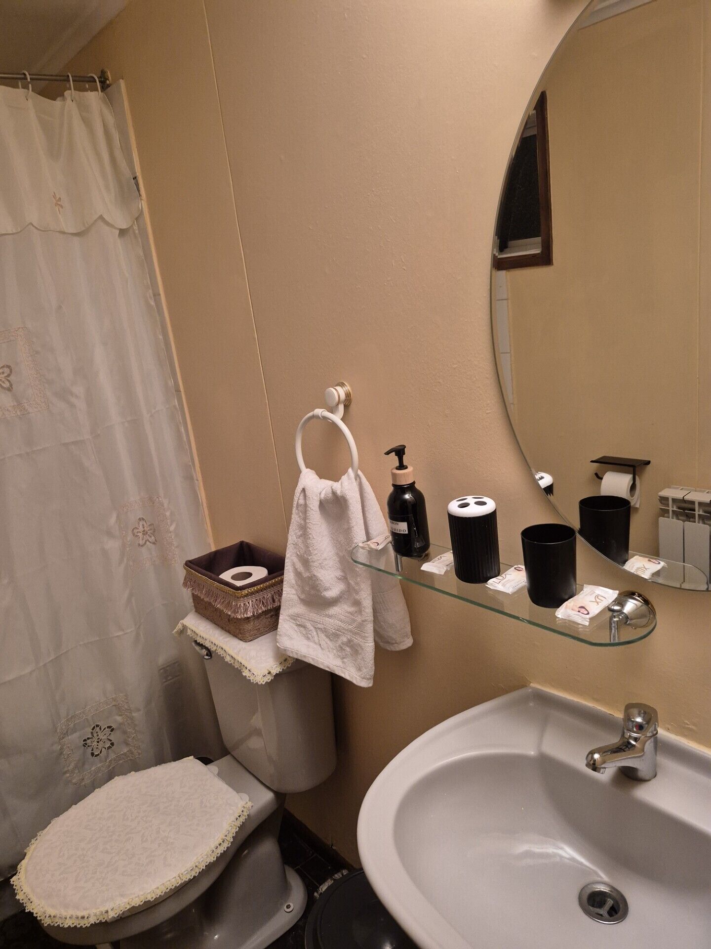 Un baño con inodoro, lavamanos y un estante de vidrio con artículos de aseo.