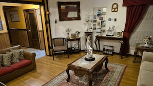 A living room with a wooden coffee table, a sofa, and a chair. There is a rug on the floor, a clock on the wall, and a mirror above the coffee table. - Hostal Oasis (Puerto Natales)