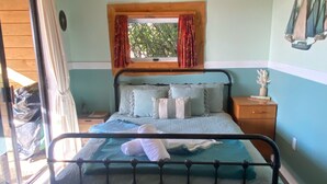 Un dormitorio con cama, mesita de noche, silla, ventana con cortinas y techo de madera.