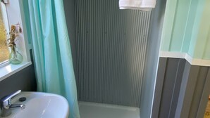 Un baño con ducha, lavabo y ventana con cortina.