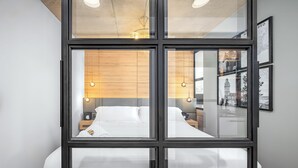 Habitación de hotel moderna con un ventanal grande, pared de paneles de madera y una cama con ropa blanca.