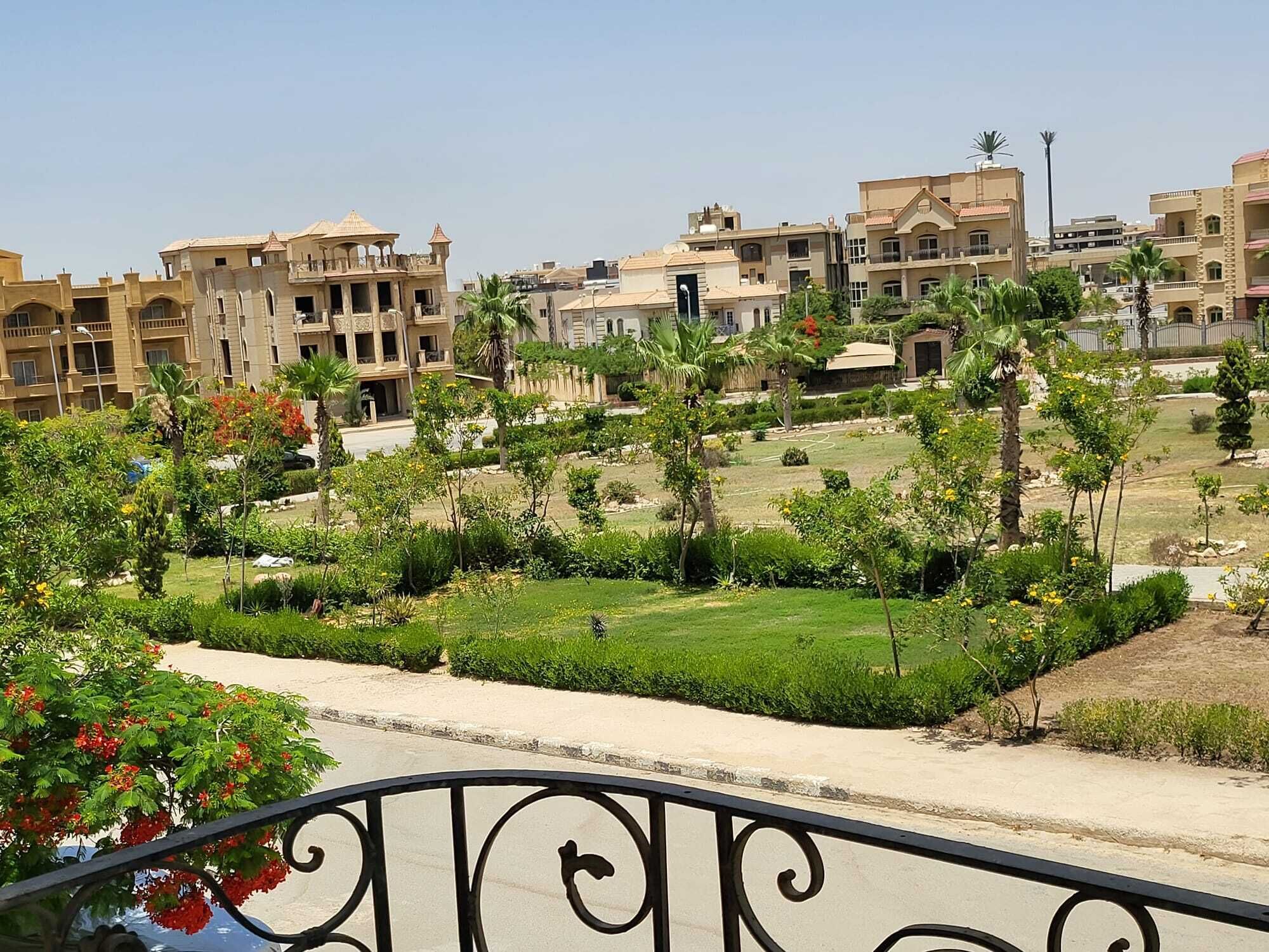Un quartier résidentiel avec des immeubles à plusieurs étages, un jardin bien entretenu avec des palmiers et un ciel dégagé.