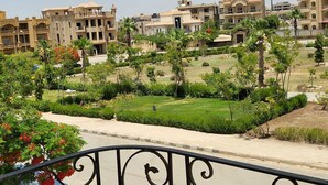 A residential area with multi-story buildings, a well-maintained garden with palm trees, and a clear sky. - Fully furnished, luxury villa located in Diplomatic Compound in New Cairo. (New Cairo)