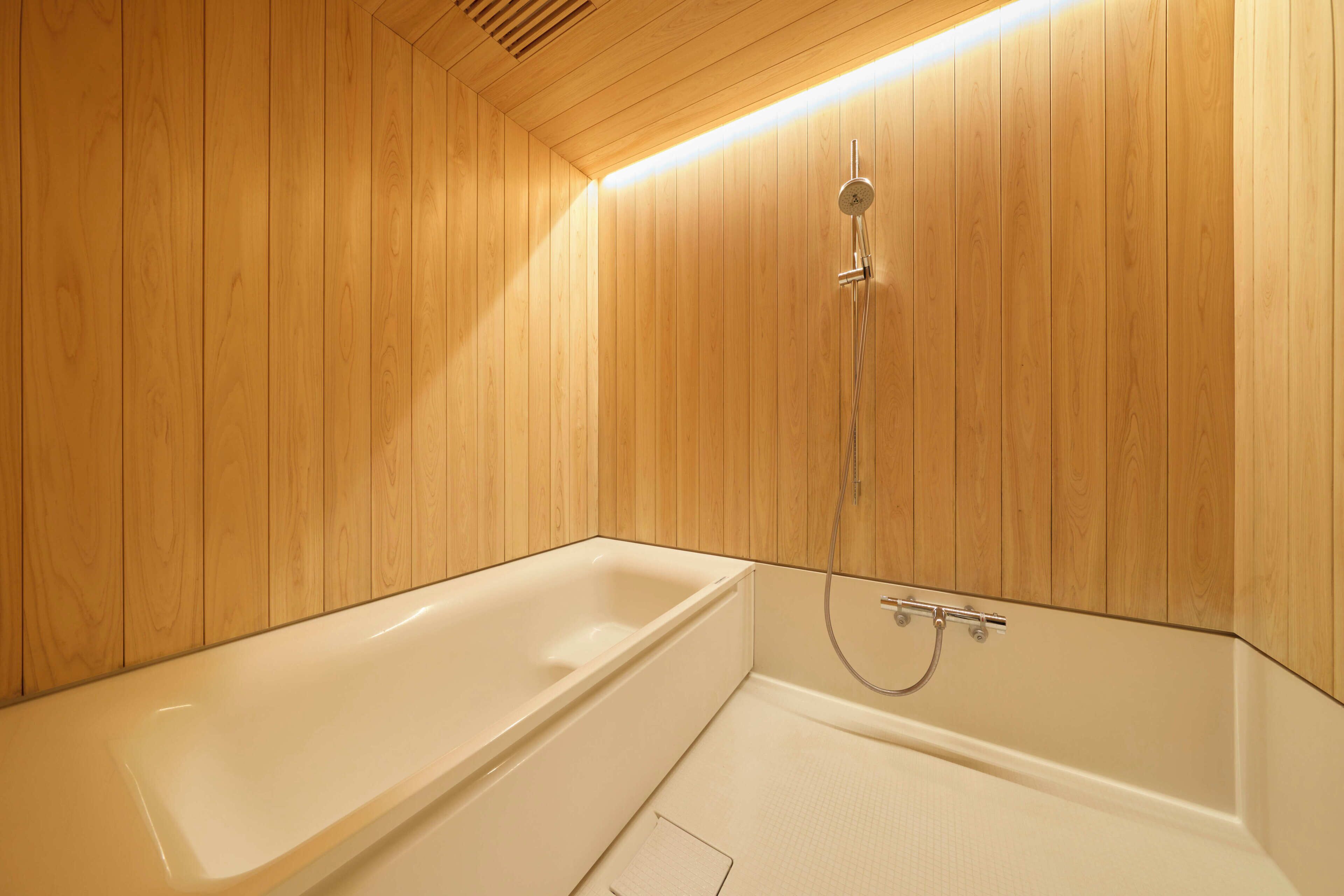 Une salle de bain aux murs lambrissés, avec une baignoire blanche et une douche.