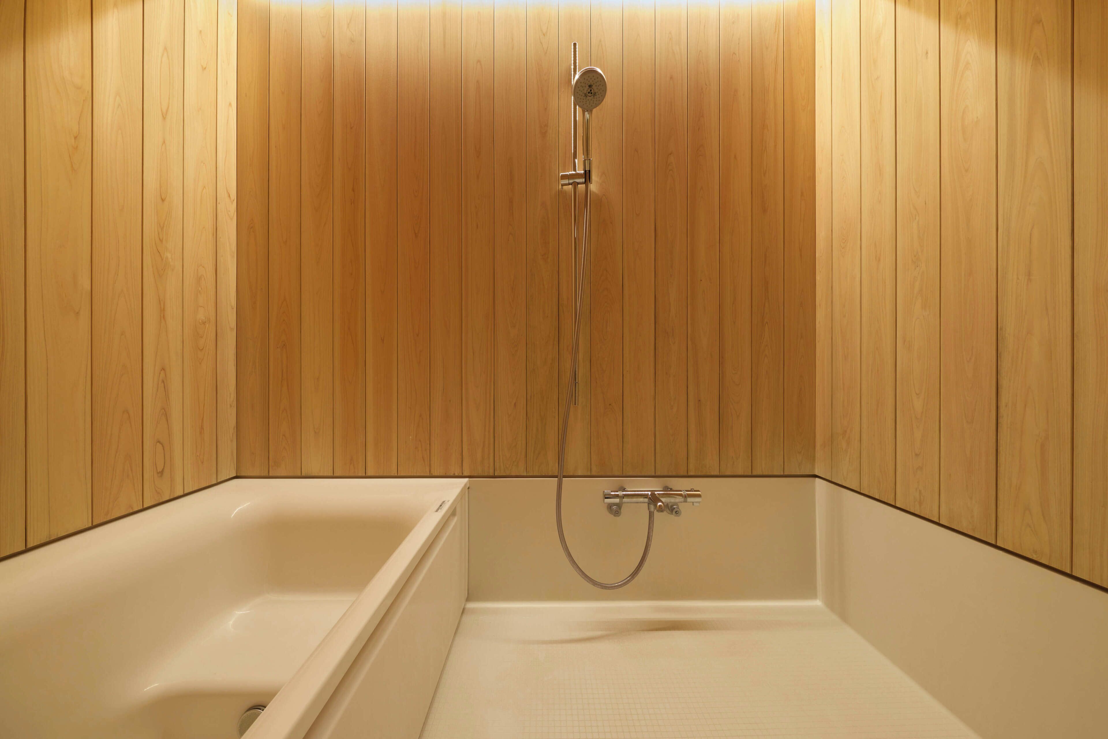 A bathroom with wooden panel walls, a bathtub, and a shower unit.