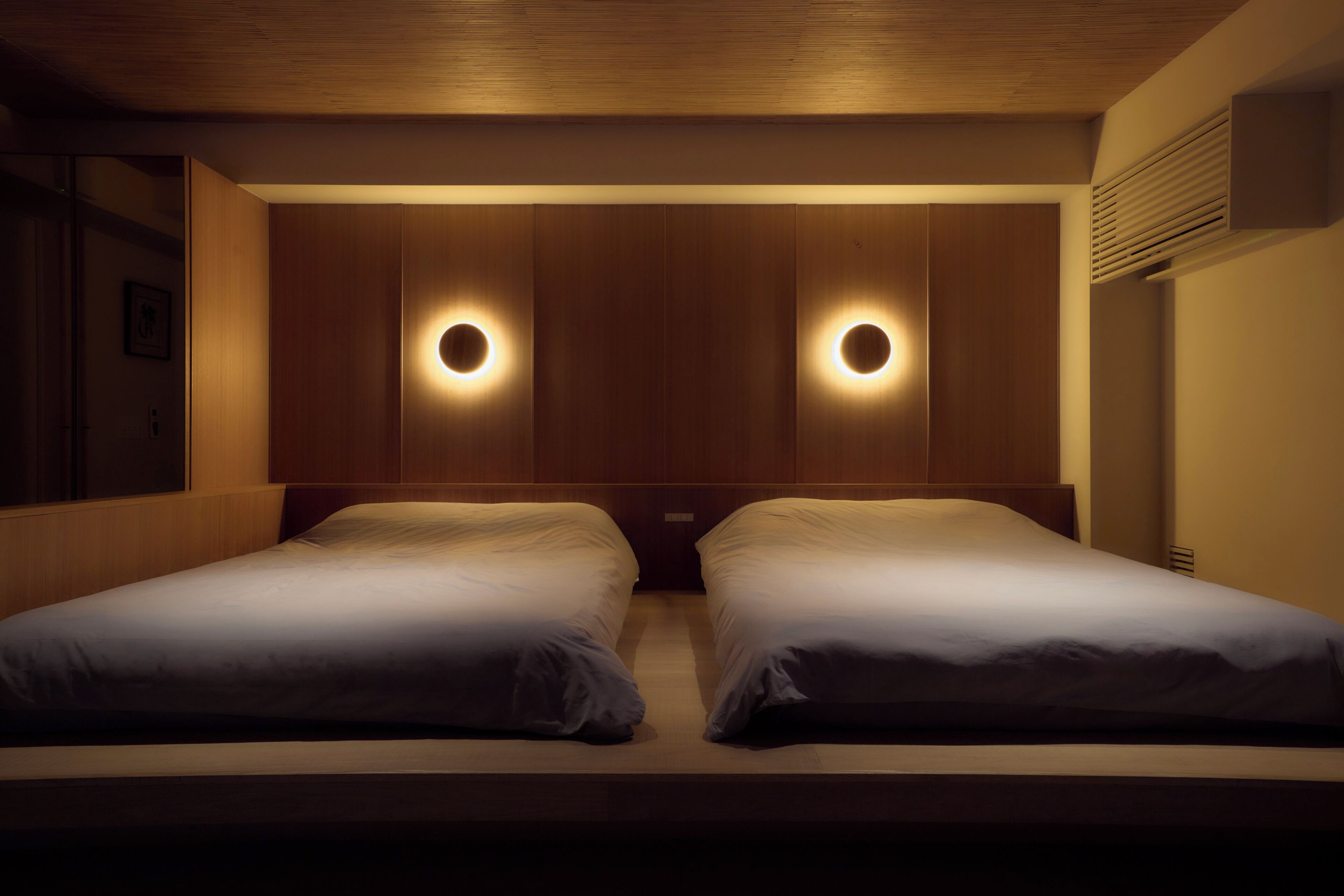 Una camera d'albergo con due letti, rivestimenti in legno sulle pareti e applique circolari.