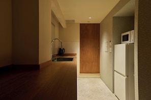 A narrow hallway with a wooden door, a white refrigerator, and a kitchen area with a microwave. - Hotel Matoma (Tokyo)