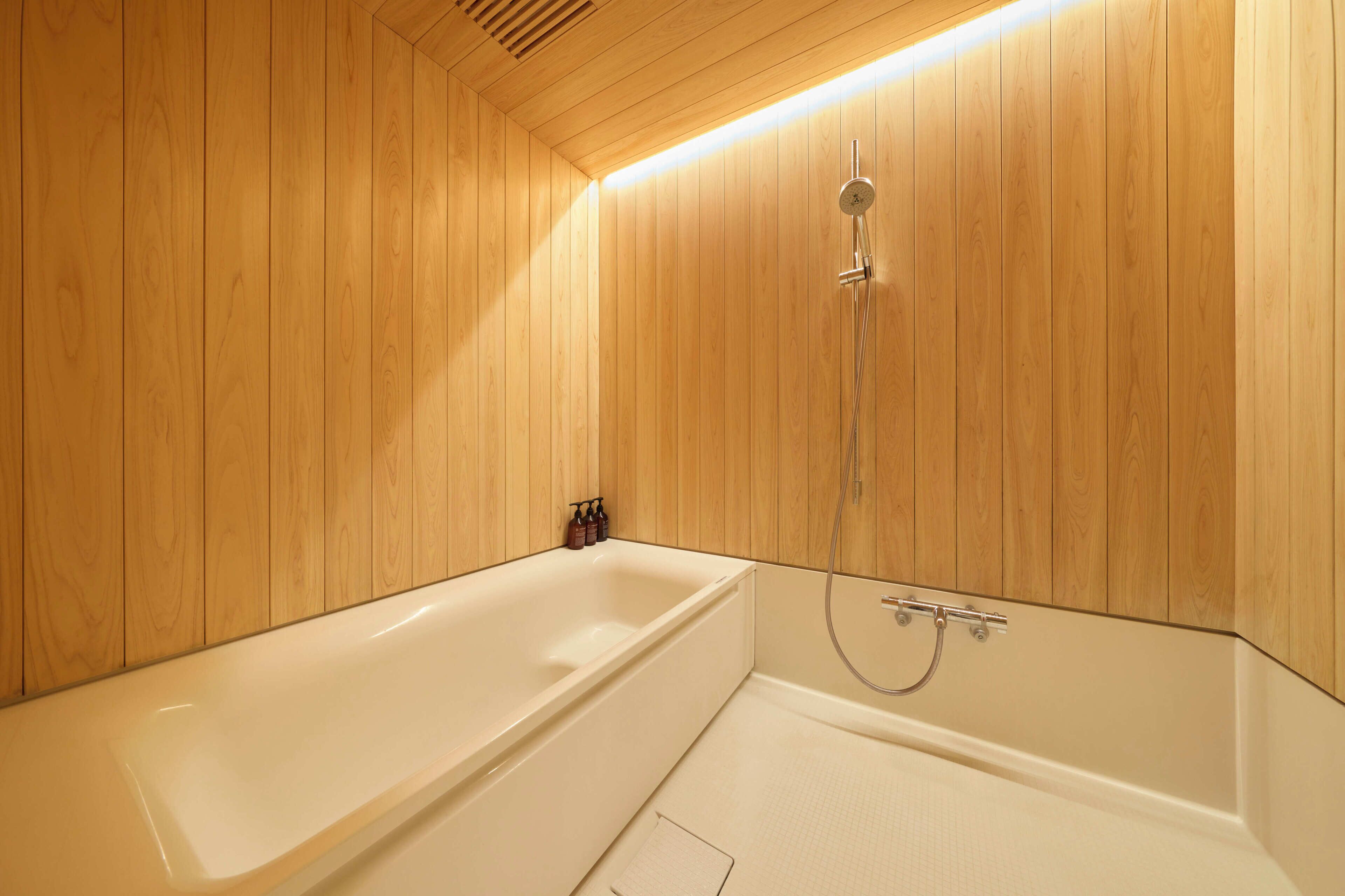 Une salle de bain aux murs lambrissés, équipée d’une baignoire et d’une douche.