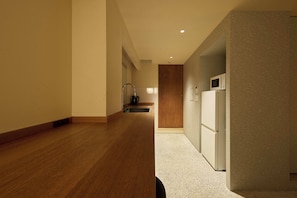 A hallway with wooden flooring, a kitchen area with a refrigerator and microwave, and a wooden door at the end. - Hotel Matoma (Tokyo)