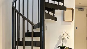 A spiral staircase with a black metal railing, a white wall, and a small white table with books and a potted plant.