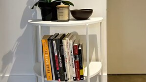 A white bookshelf with books and a potted orchid.